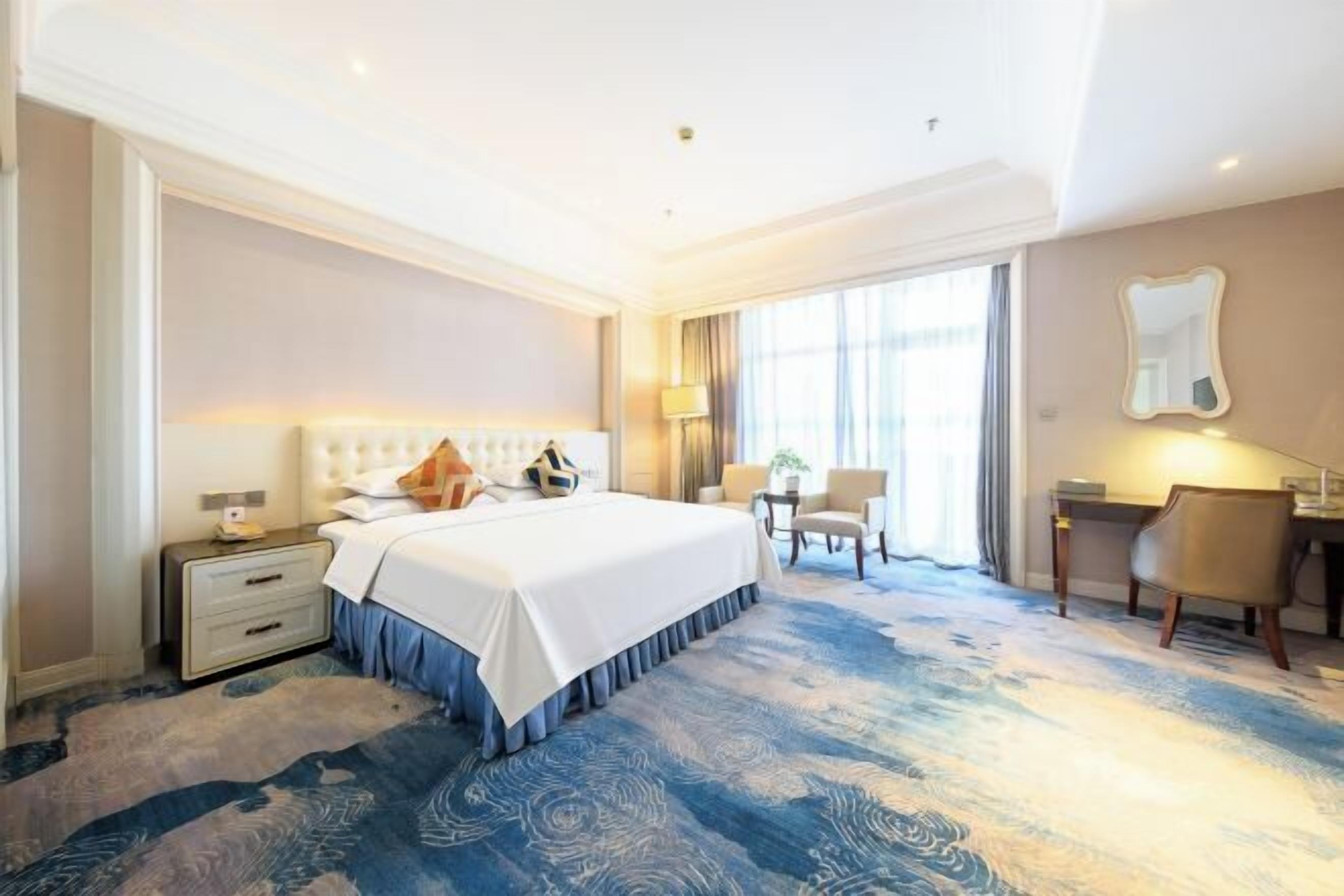 A hotel room with a large bed, bedside tables, a desk, and a chair.