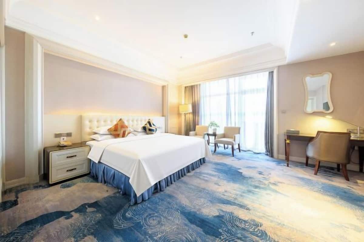A hotel room with a large bed, bedside tables, a desk, and a chair.
