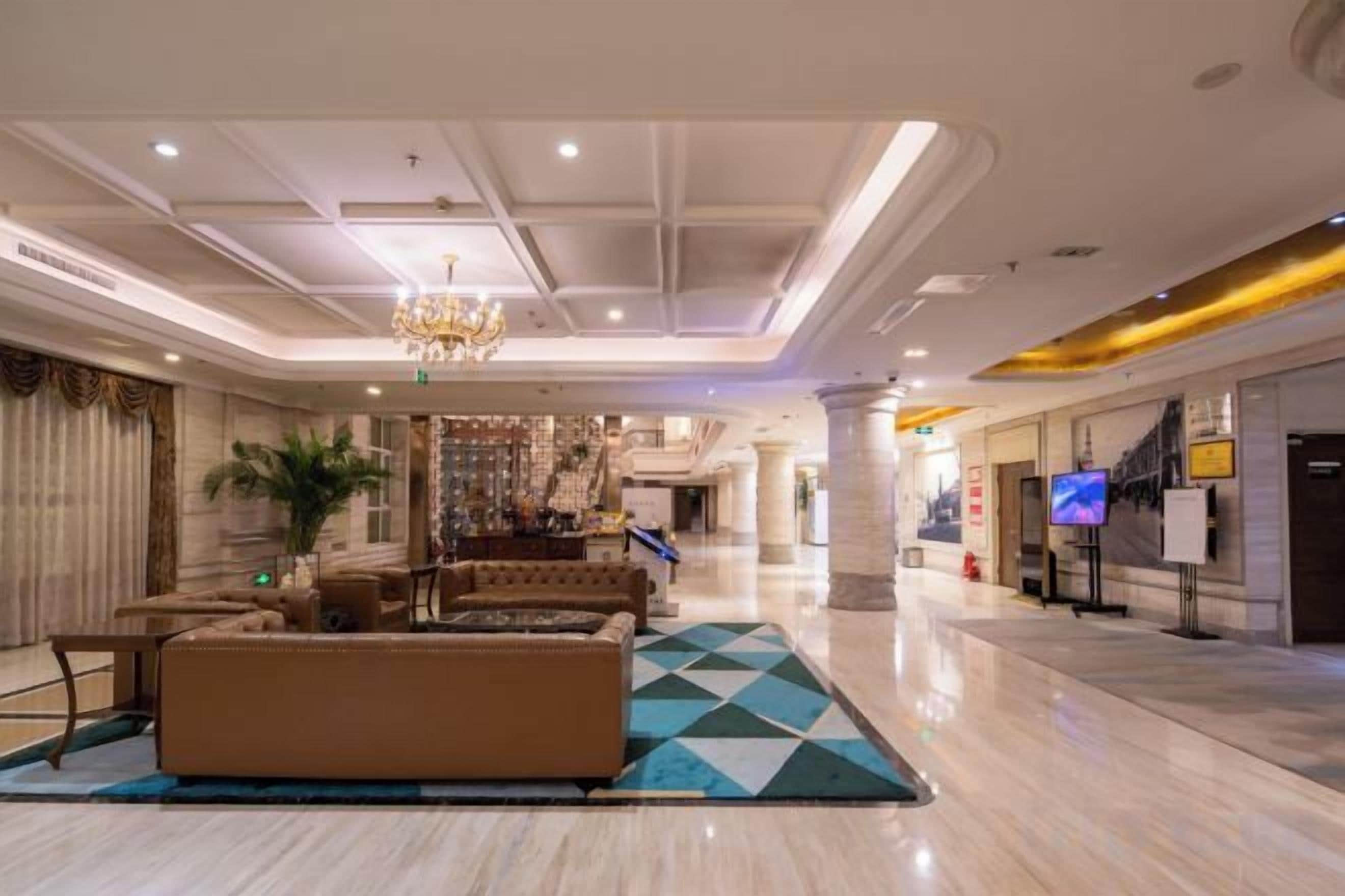 A spacious lobby with a large sofa, a chandelier, and a television screen.