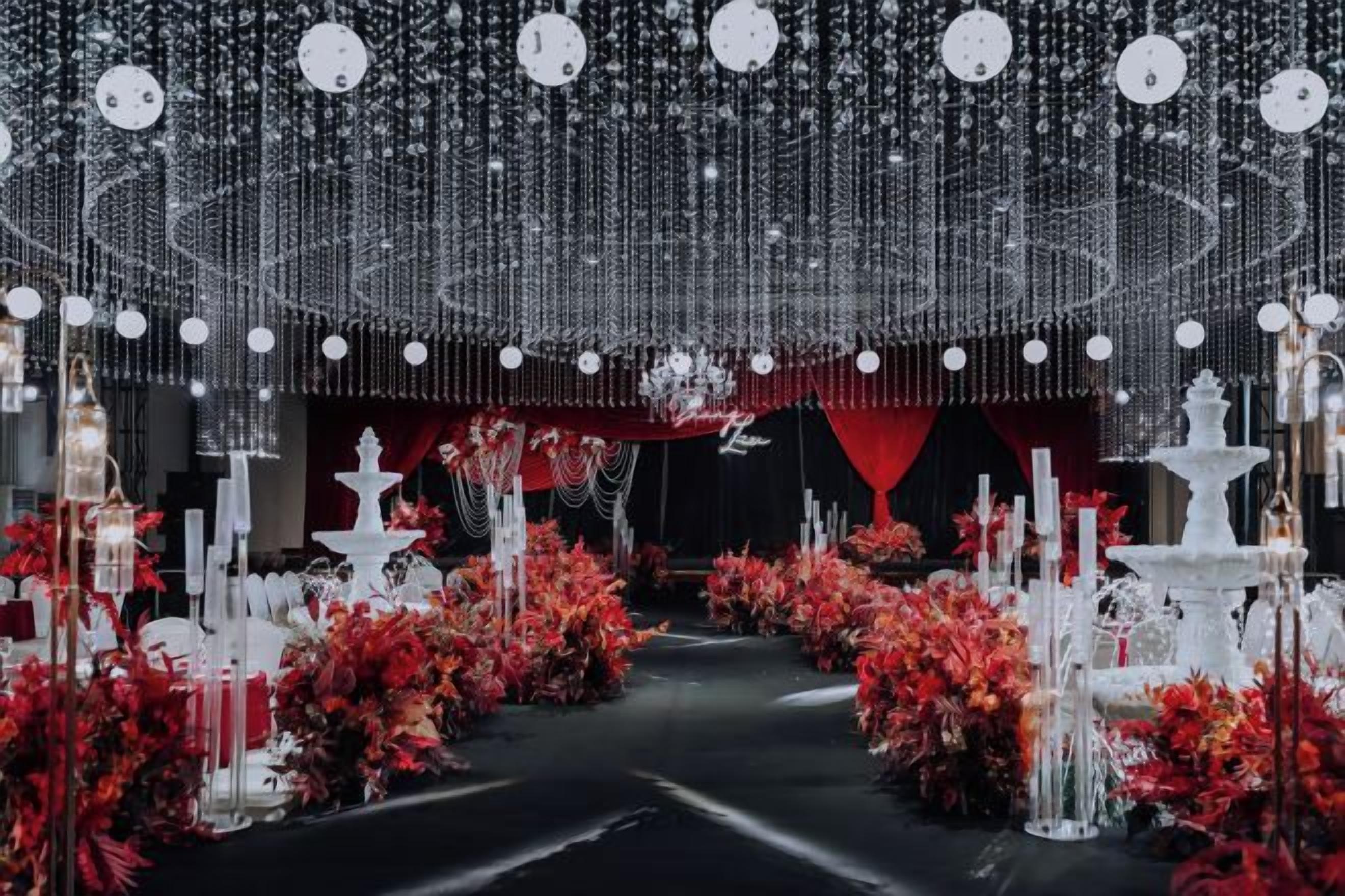 An indoor venue with a central aisle, red floral arrangements, and hanging light fixtures.