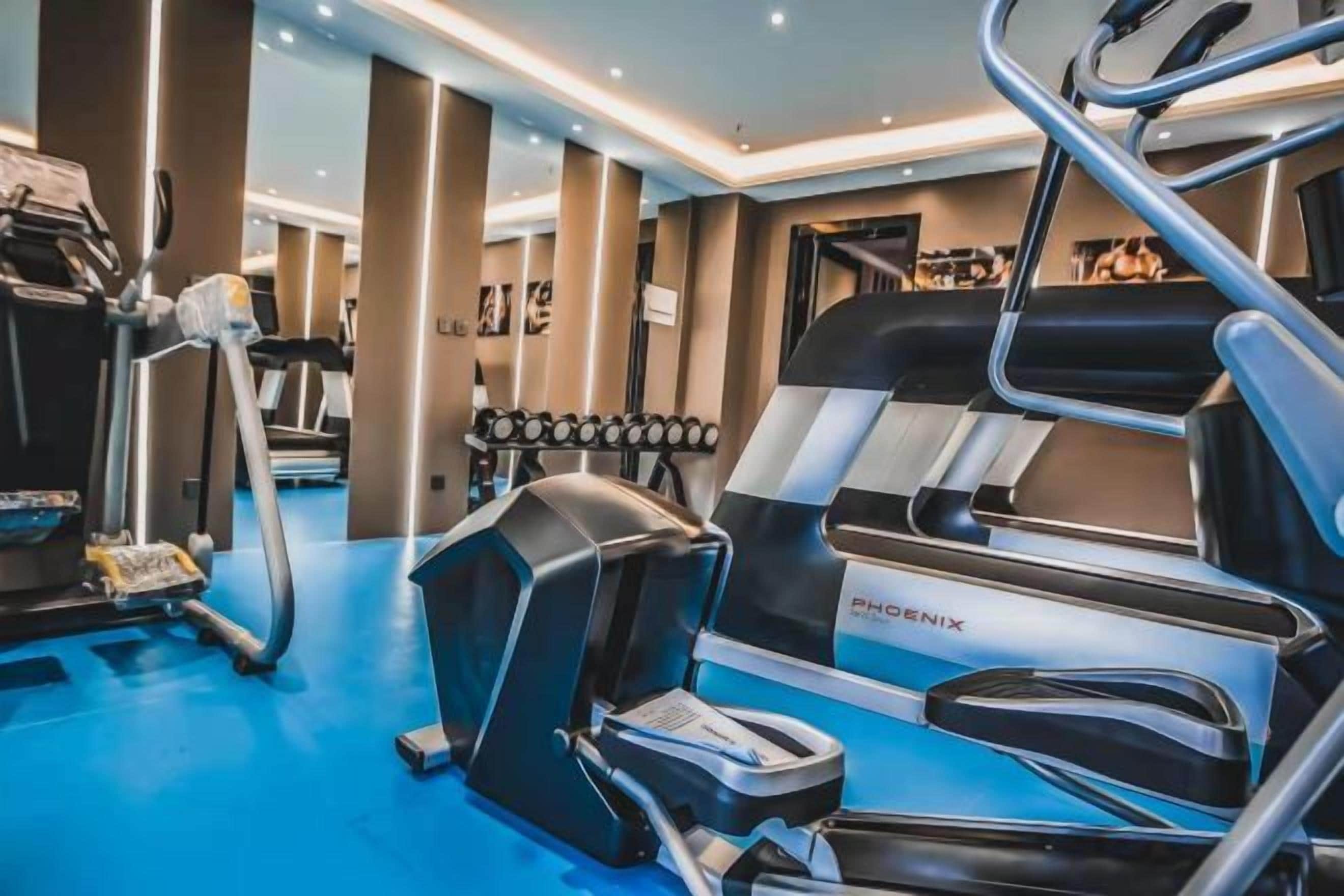 Un gimnasio con equipamiento de ejercicios, incluyendo una cinta de correr, elíptica y pesas.