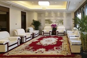 A hotel lobby with a red carpet, white sofas, and a large mirror.