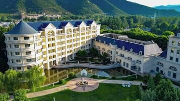 A large hotel with multiple buildings, a central courtyard, and a surrounding lush green landscape.