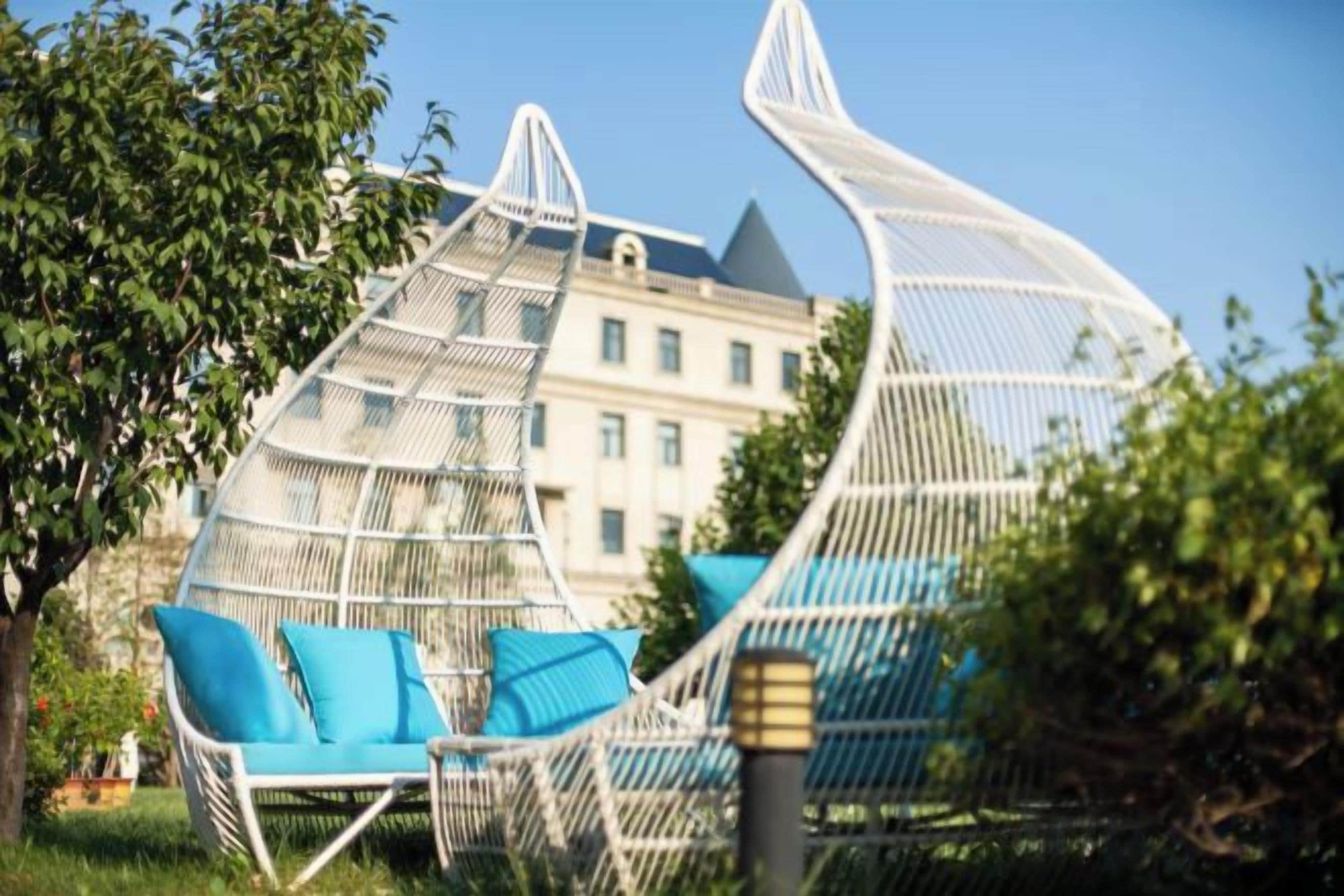 A white, curved, net-like structure with a blue cushioned chair in front.