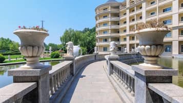 A bridge with ornate stone railings and two large flower pots, leading to a multi-story building with balconies.