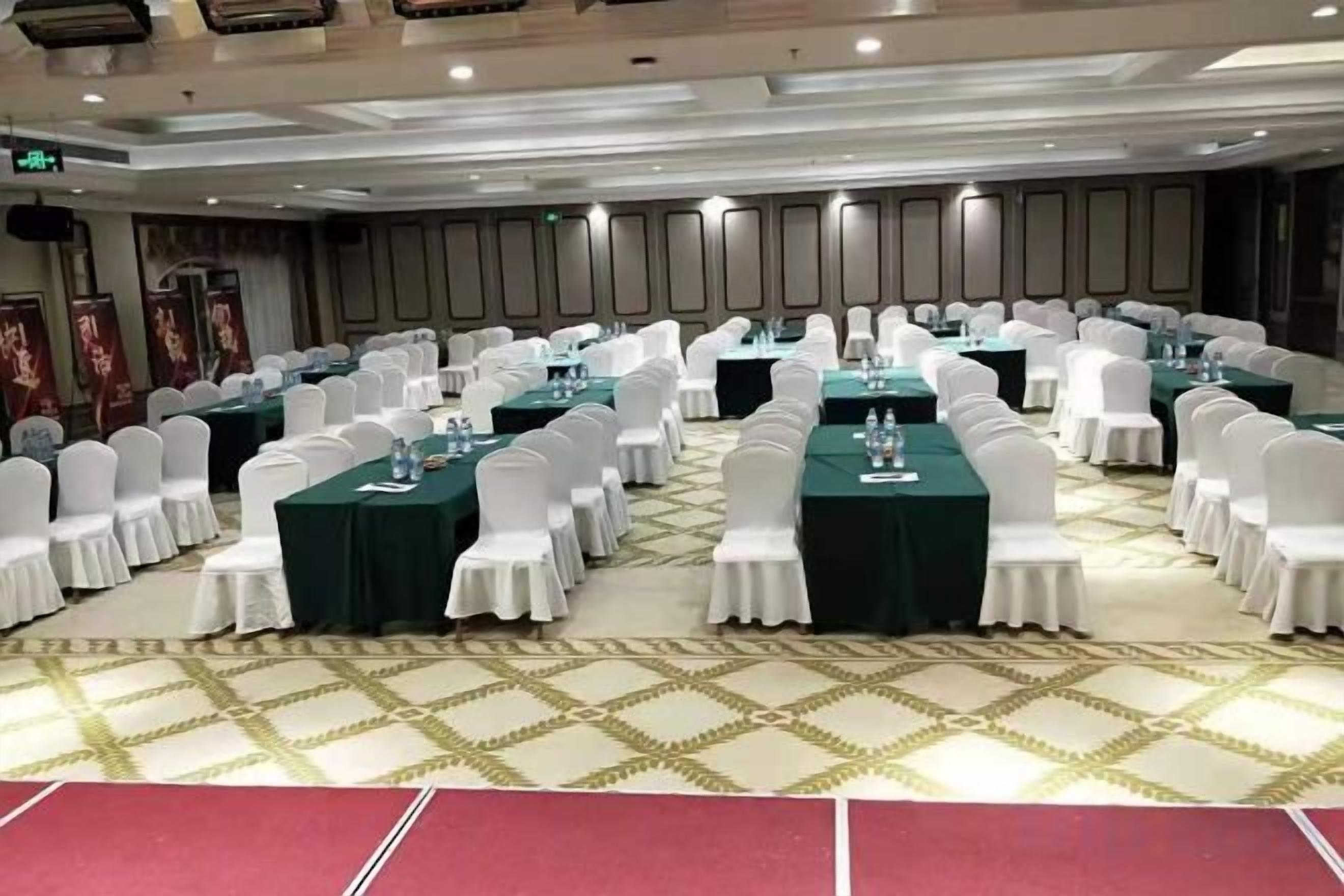 Un salón de conferencias con mesas redondas, sillas blancas y manteles verdes.
