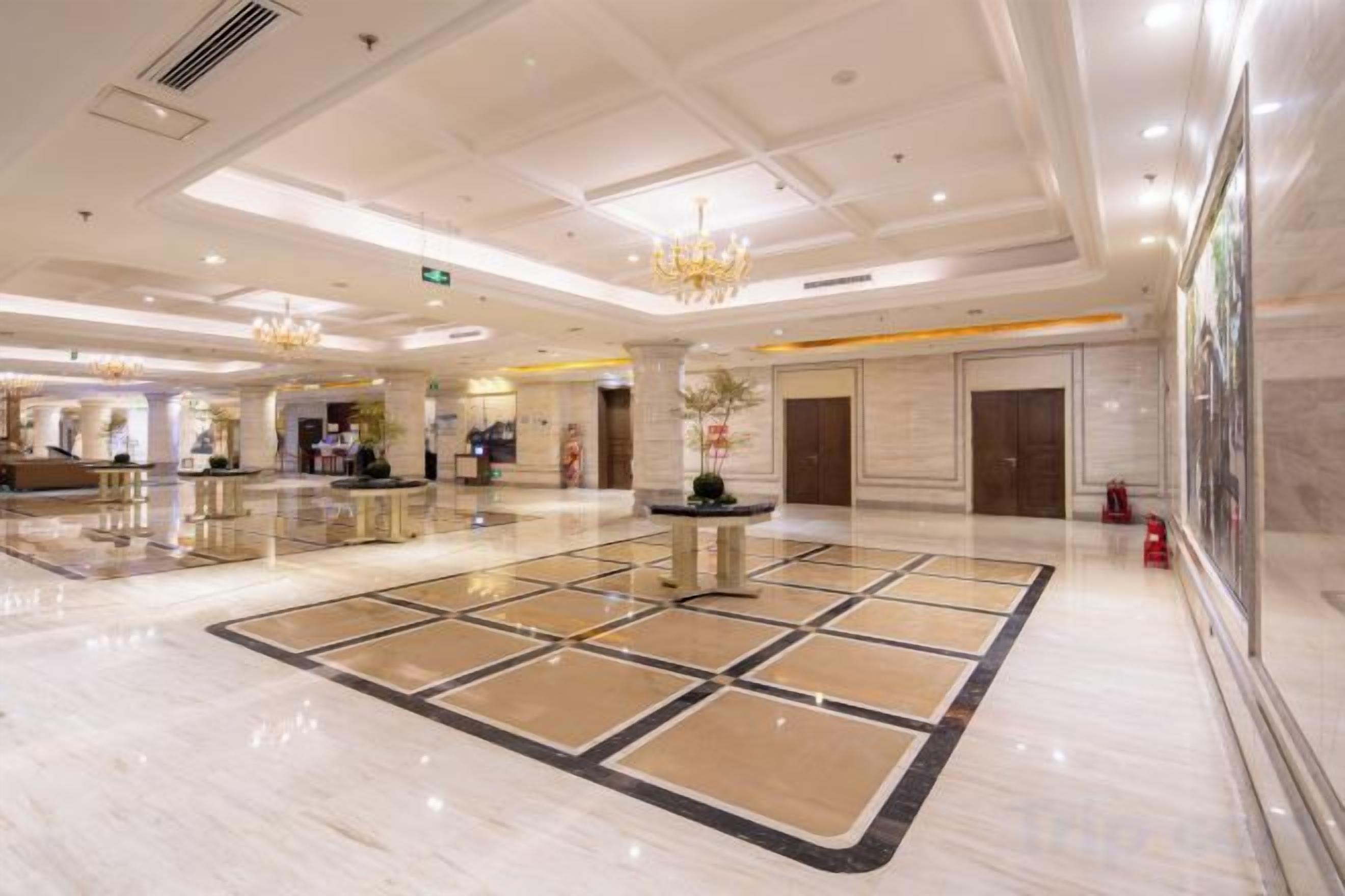 Een ruime lobby met een gepolijste marmeren vloer, een receptiebalie en een kroonluchter.