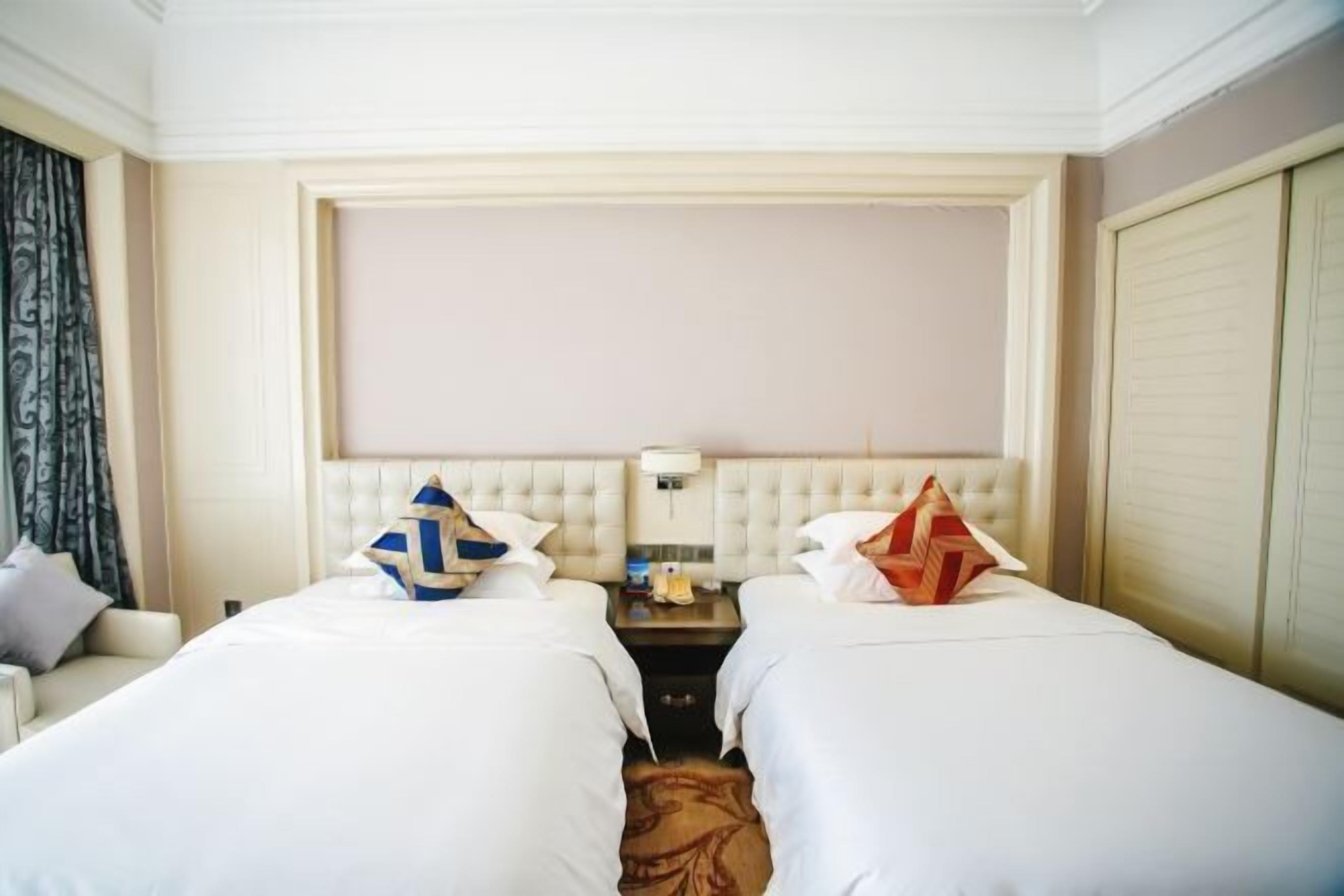 A hotel room with two beds, a nightstand, a lamp, and a wardrobe.
