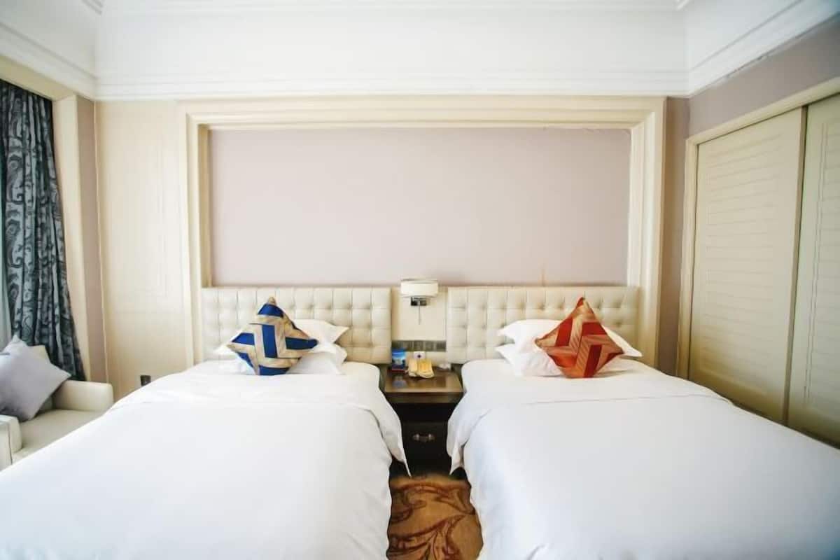 A hotel room with two beds, a nightstand, a lamp, and a wardrobe.