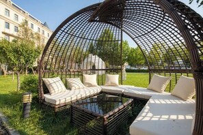 A semi-enclosed outdoor seating area with a cushioned bench and a glass table, surrounded by a lattice structure.