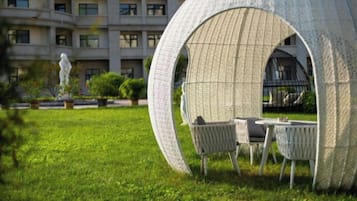 A circular structure with seating, surrounded by a grassy area and a building in the background.