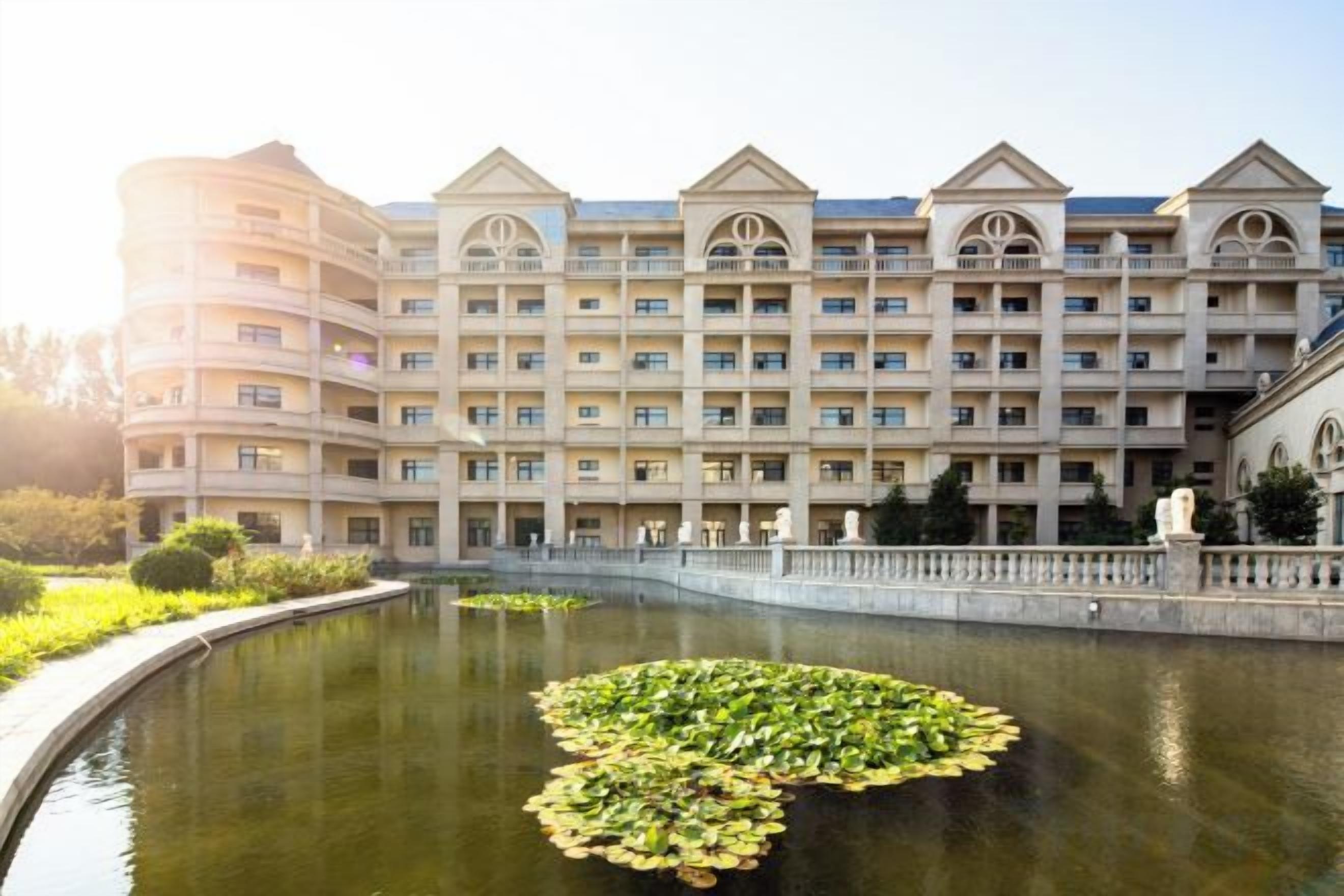 A multi-story hotel with a courtyard featuring a pond with lily pads.