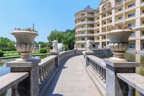 A bridge with ornate stone balustrades, a body of water, and a multi-story building with balconies in the background.