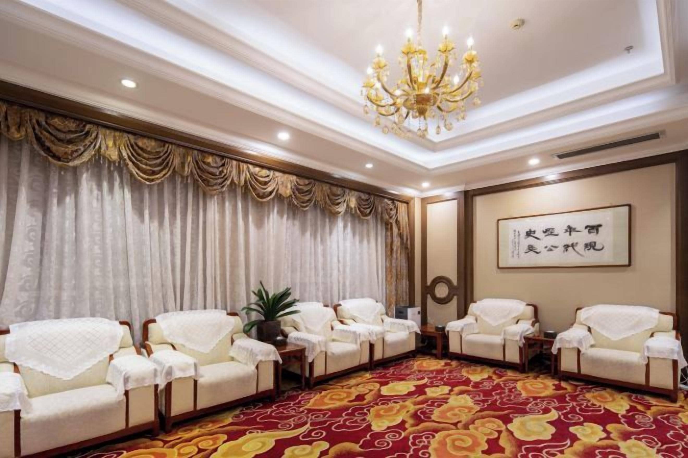 A conference room with a red carpet, white chairs, a chandelier, and a framed artwork on the wall.