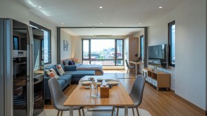 A modern living room with a sofa, dining table, chairs, a TV, and a city view. - HoLo Giang Vo Hanoi - Serviced HomeStay (Hanoi)