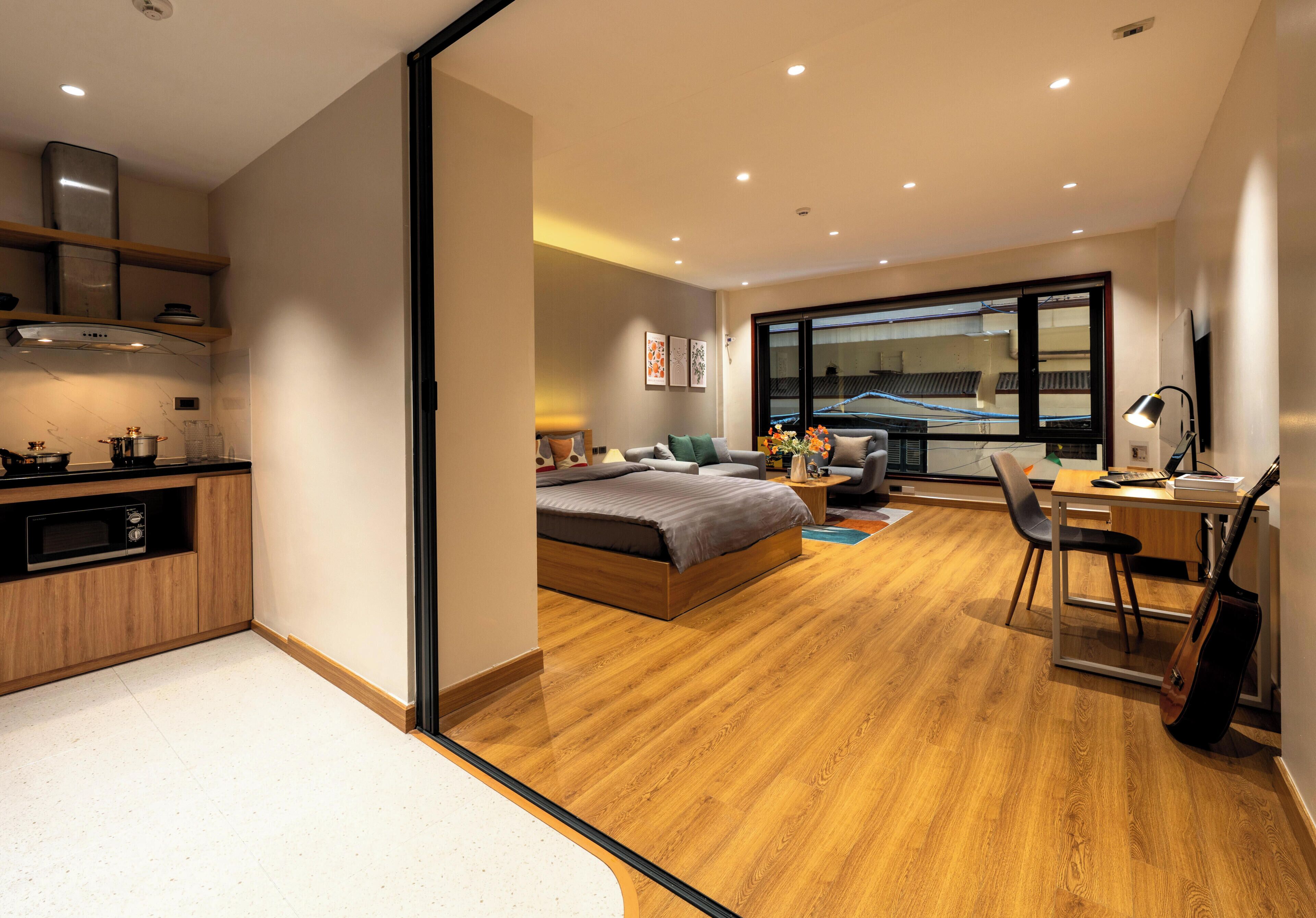 Une chambre d’hôtel moderne avec un plancher en bois, un lit, un bureau avec une chaise, une guitare et une grande fenêtre.