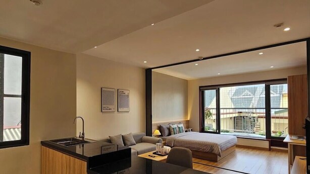 A modern hotel room with a kitchenette, a bed, a sofa, and large windows. - HoLo Giang Vo Hanoi - Serviced HomeStay (Hanoi)