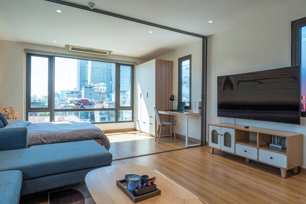 A modern bedroom with a large bed, a desk, a TV, and a view of the city. - HoLo Giang Vo Hanoi - Serviced HomeStay (Hanoi)