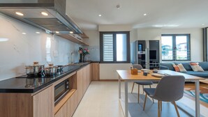 A modern kitchen with a dining area, a sofa, and a window with blinds. - HoLo Giang Vo Hanoi - Serviced HomeStay (Hanoi)