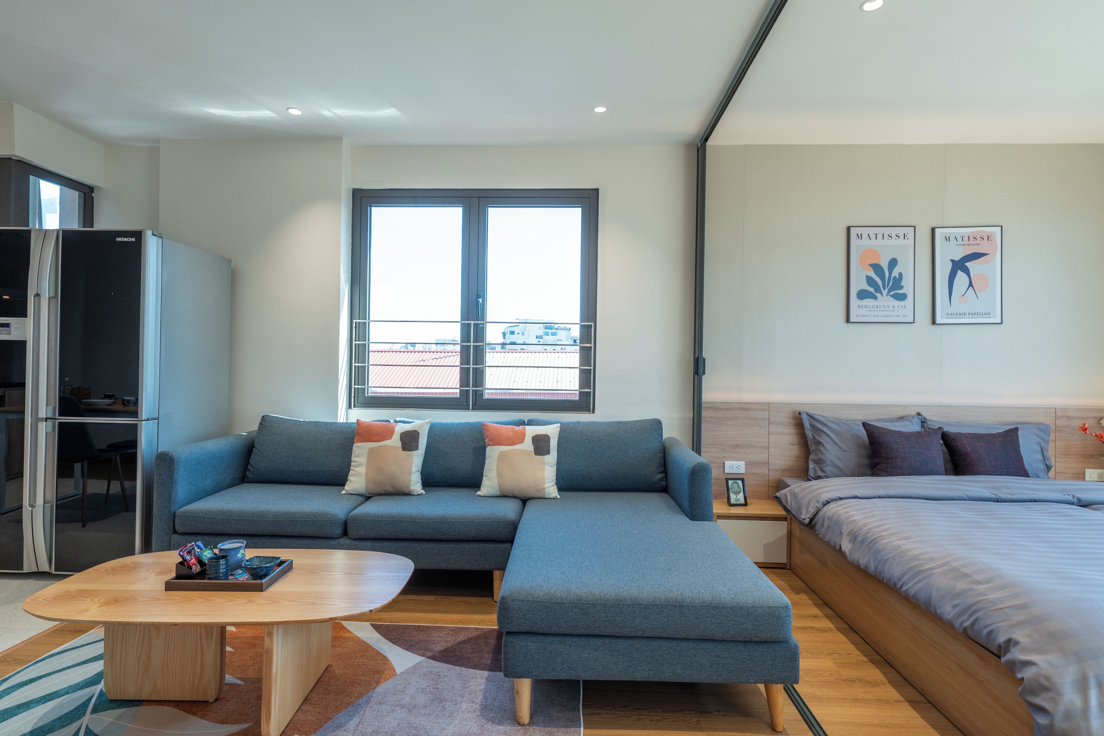 A modern hotel room with a sofa, a bed, a dining table, and a refrigerator.