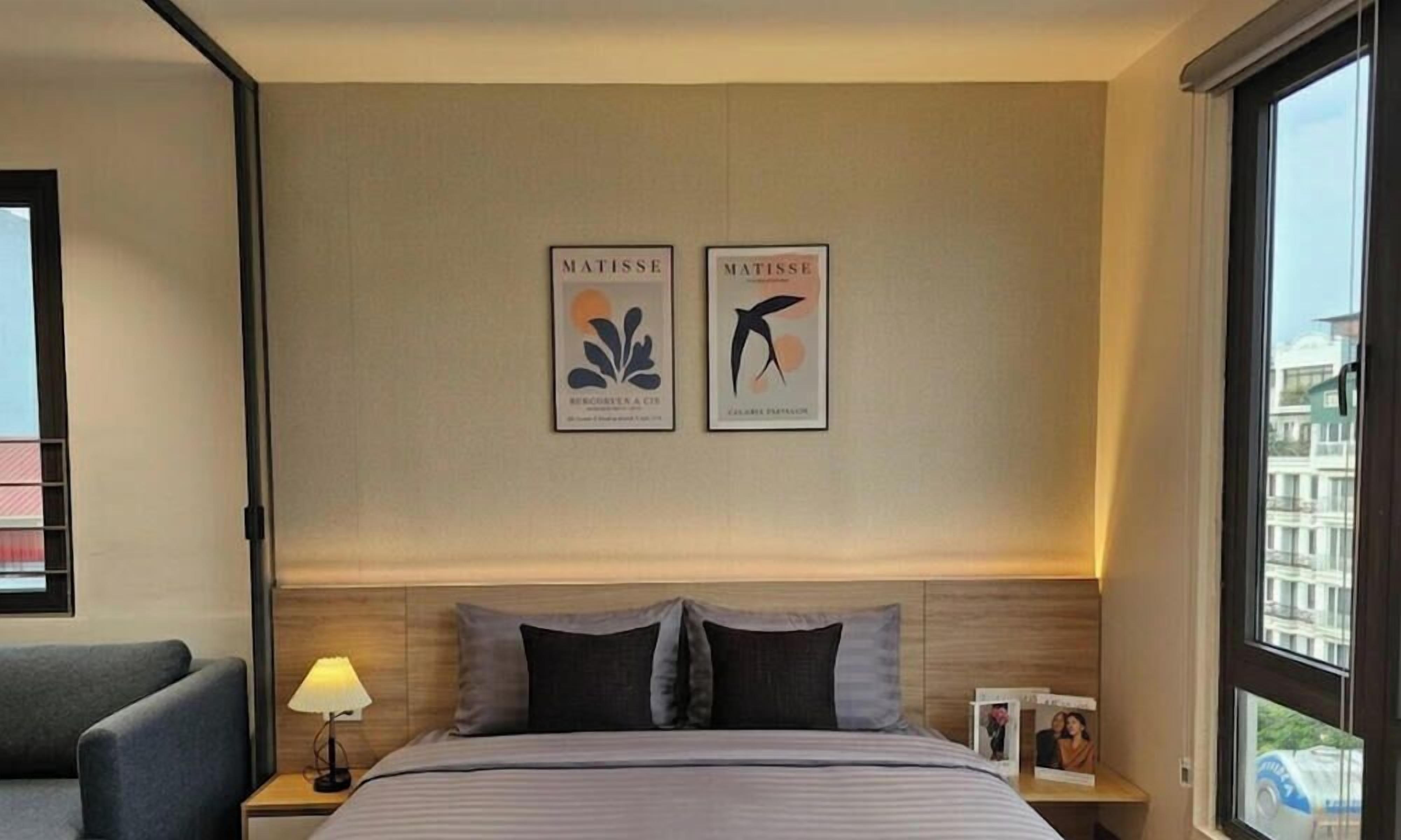 Ein Hotelzimmer mit einem Bett, einem Nachttisch, einer Lampe und zwei gerahmten Kunstwerken an der Wand.