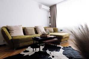 A living room with a sofa, a coffee table, a rug, and a wall-mounted air conditioner. - Alma Residence Vibrant City Center Bucharest (București)