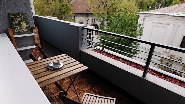 Un balcón con una mesa y sillas, un letrero que dice 'Open 24 Hours Main Street Coffee' y vista de un edificio con techo rojo.