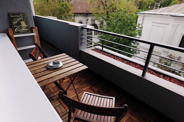 A balcony with a table and chairs, a sign with 'Open 24 Hours Main Street Coffee,' and a view of a building with a red roof. - Alma Residence Vibrant City Center Bucharest (București)