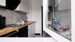 Una cocina moderna con encimera de madera, campana extractora negra y puerta de cristal que da a un comedor con platos de colores.