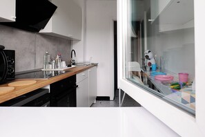 A modern kitchen with a wooden countertop, a black range hood, and a glass door leading to a dining area with colorful plates. - Alma Residence Vibrant City Center Bucharest (București)
