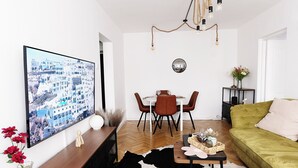 Un salón con televisor de pantalla plana, una mesa de comedor con sillas, un sofá verde y un tapete de cuero de vaca.