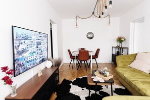 A living room with a flat-screen TV, a dining table with chairs, a green sofa, and a cowhide rug. - Alma Residence Vibrant City Center Bucharest (București)