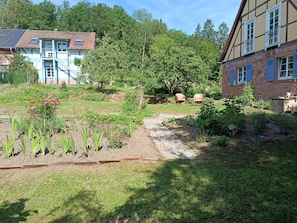 Ein Garten mit einem Pfad, zwei Häuser mit traditioneller Architektur und verschiedenen Pflanzen.