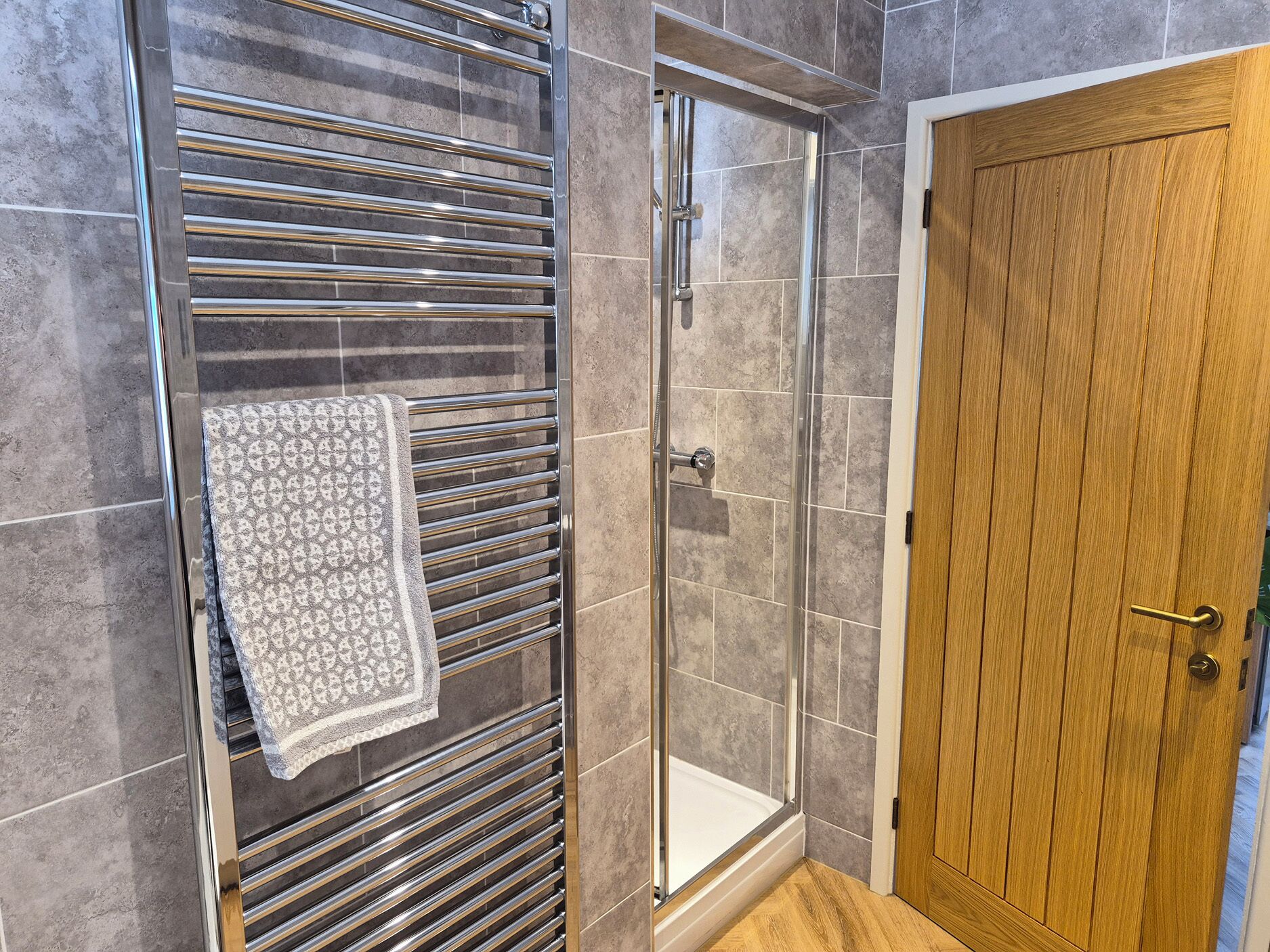 A shower with a glass door, a towel hanging on a metal rack, and a wooden door.