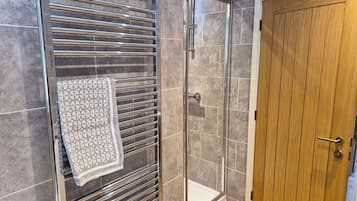 A shower with a glass door, a towel hanging on a metal rack, and a wooden door.