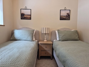 A bedroom with two single beds, a nightstand with a lamp, and two framed pictures on the wall. - Thorn Tree Cottage (Hope Valley)