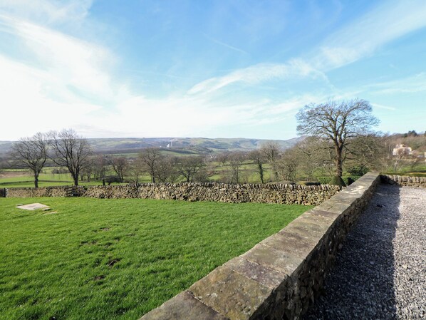 A stone wall with a grassy field, trees, and a distant view of hills. - Thorn Tree Cottage (Hope Valley)