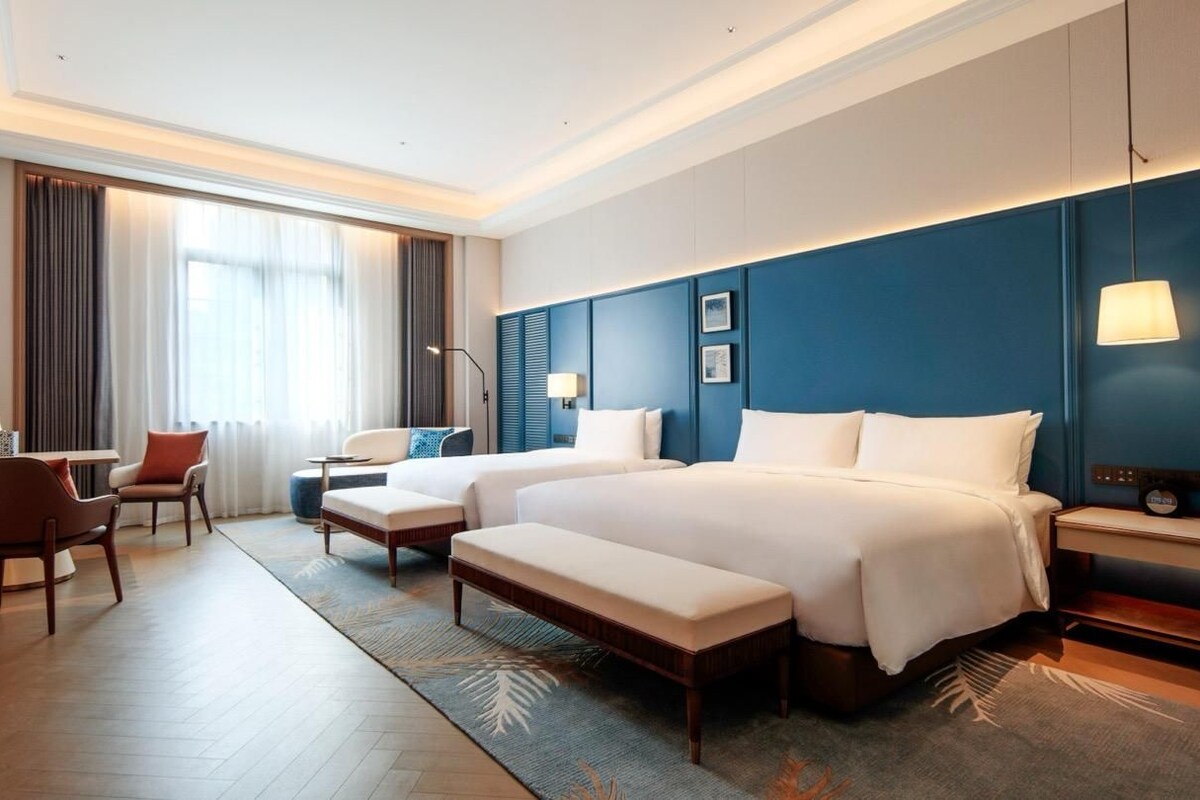 A hotel room with a large bed, a desk, a chair, and a lamp.