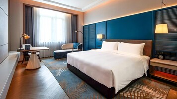 A hotel room with a large bed, a desk, a chair, and a television.