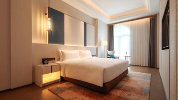 Una habitación de hotel moderna con una cama grande, mesitas de noche, una lámpara de pared y vistas al exterior a través de la ventana.