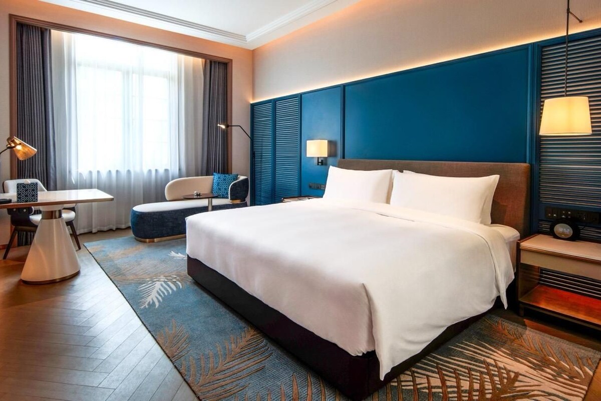 A hotel room with a large bed, a desk, a chair, and a television.