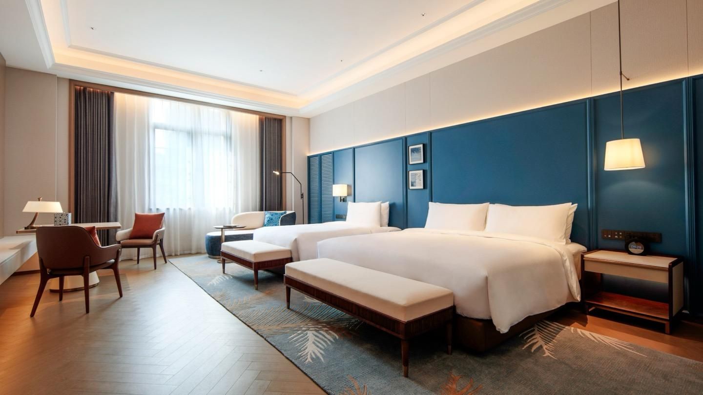 A hotel room with a large bed, a desk, a chair, and a lamp.