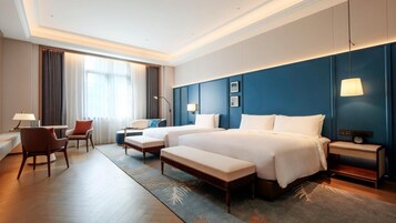 A hotel room with a large bed, a desk, a chair, and a lamp.