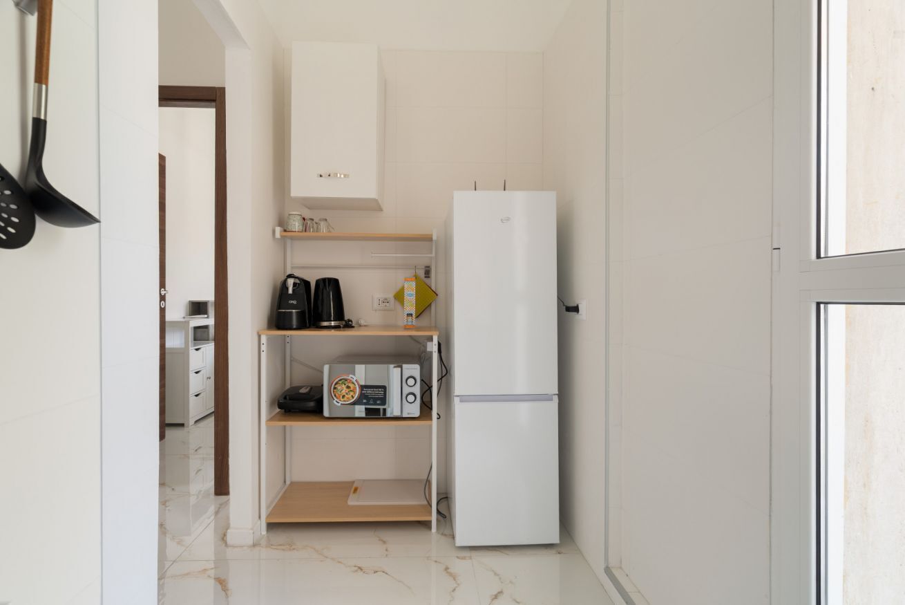 Eine kleine Küche mit einem weißen Kühlschrank, einer Mikrowelle und einer Kaffeemaschine auf einem Regal.