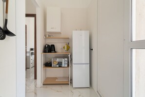 Eine kleine Küche mit einem weißen Kühlschrank, einer Mikrowelle und einer Kaffeemaschine auf einem Regal.