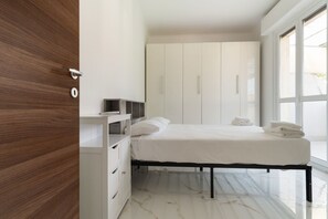 Ein modernes Schlafzimmer mit Bett, weißem Kleiderschrank und einem Fenster.