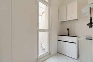 Eine kleine Küche mit weißen Schränken, einem schwarzen Wasserhahn und einem Fenster.