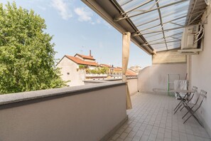 Ein Balkon mit Blick auf Häuser und Bäume, ein Tisch mit Stühlen und eine Klimaanlage.