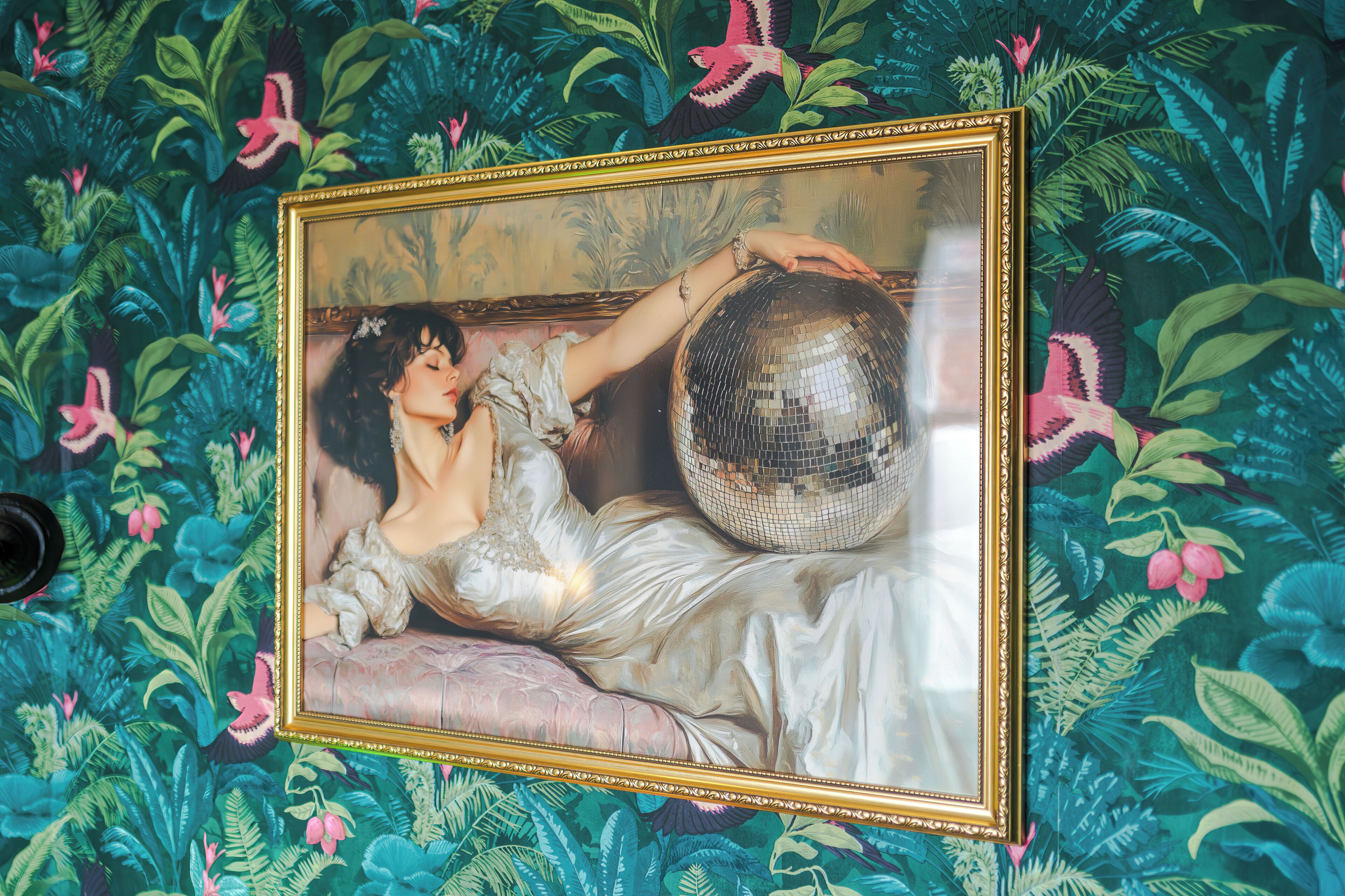 A framed artwork with a woman and a disco ball on a wall with a floral pattern.