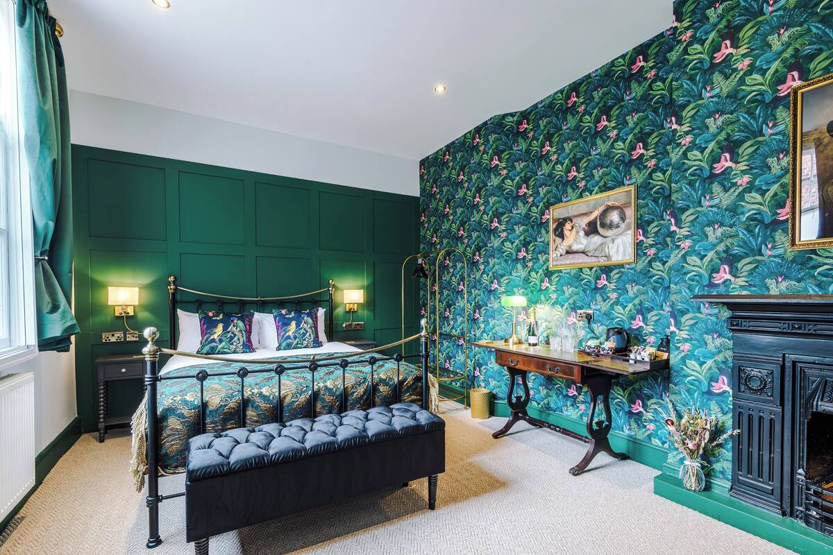A bedroom with a four-poster bed, a bench, a nightstand, a dresser, a mirror, and a fireplace.